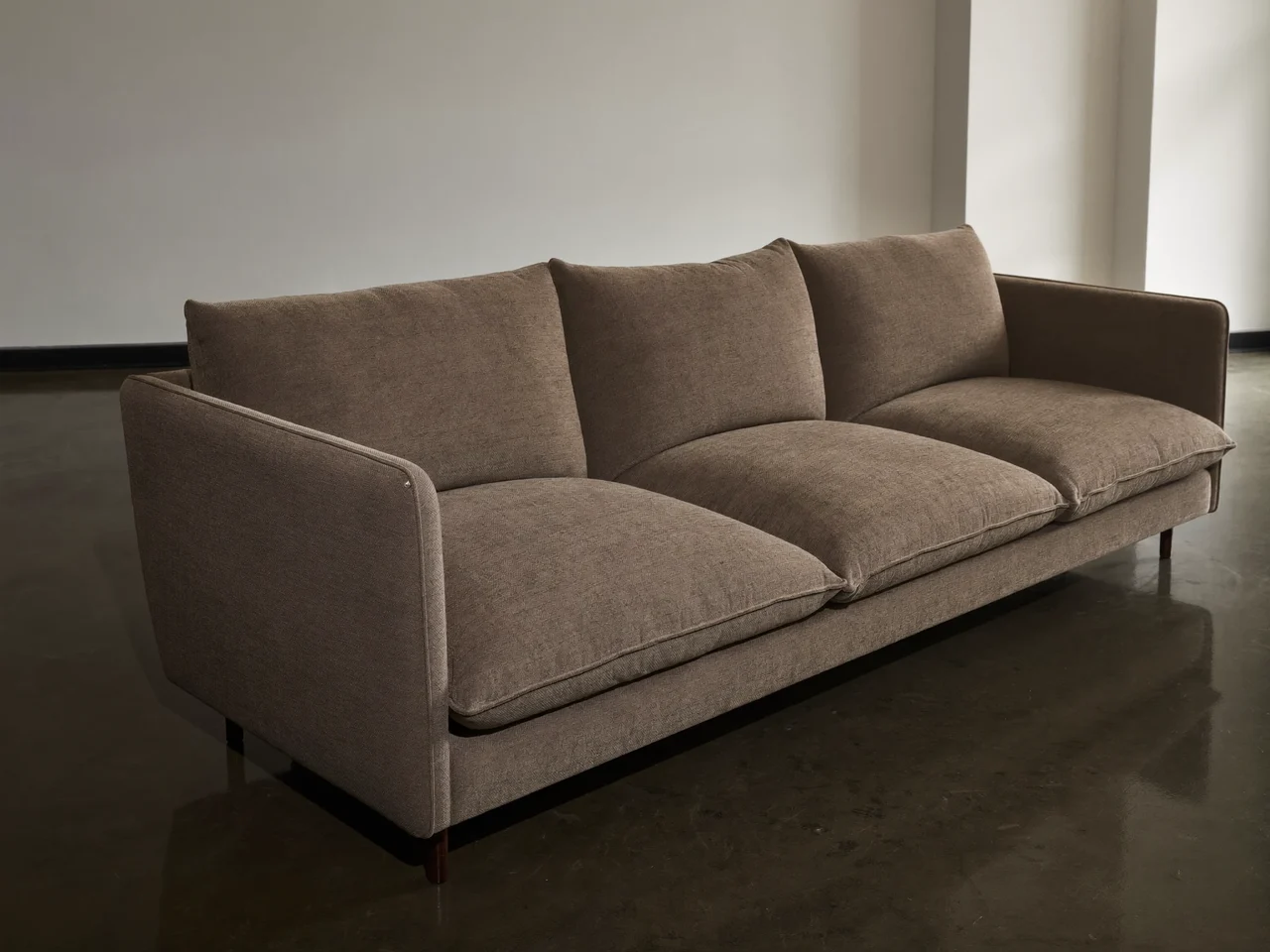 Trzyosobowa sofa w neutralnej tkaninie przy gładkiej ścianie