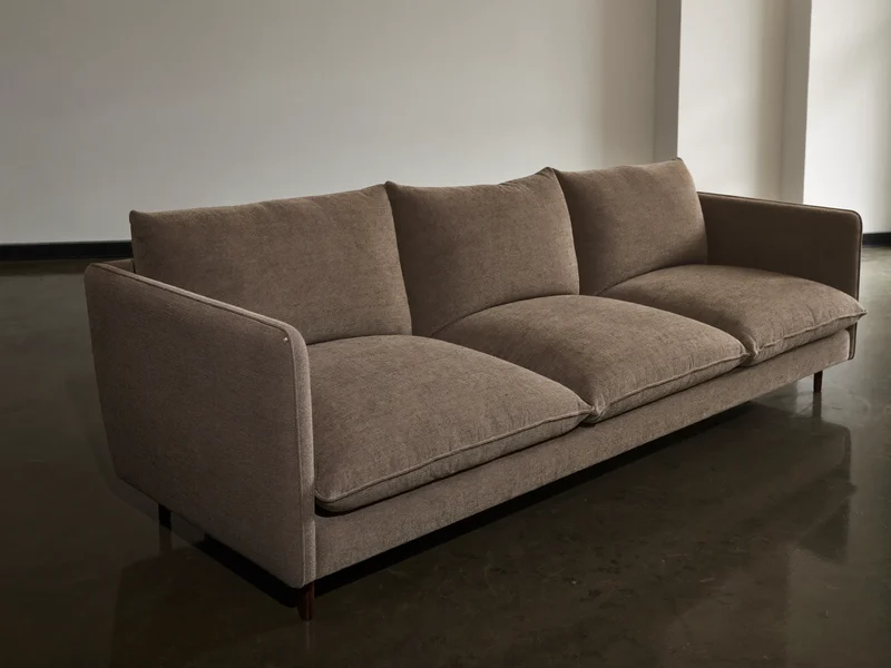 Trzyosobowa sofa w neutralnej tkaninie przy gładkiej ścianie